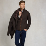 Man wearing a brown jacket over a dark shirt with a neutral background