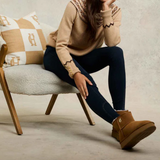 Person wearing a beige sweater and brown boots sitting on a chair with a patterned pillow.