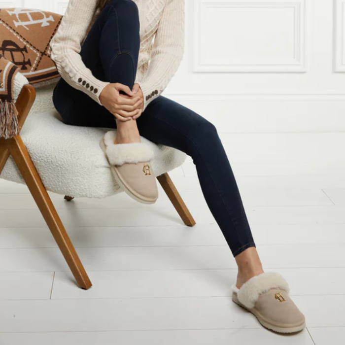 Person wearing beige slippers with a fluffy interior, sitting on a chair.