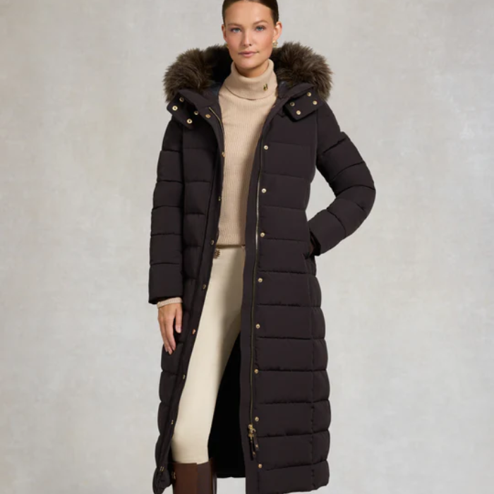 Woman wearing a long dark brown puffer coat with a fur-lined hood on a plain background