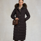 Woman wearing a long dark brown puffer coat and a brown over the shoulder leather bag on a beige background