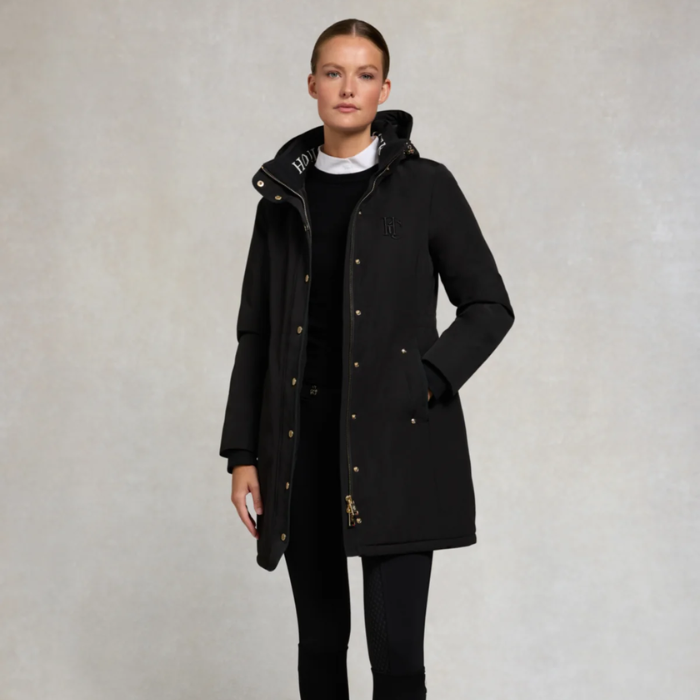 Woman wearing a black coat with a hood against a plain background