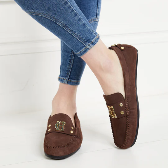 Brown loafers with gold accents worn with blue jeans on a white background