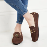 Brown loafers with gold accents worn with blue jeans on a white background