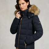Woman wearing a navy blue puffer jacket with a fur-lined hood on a neutral background