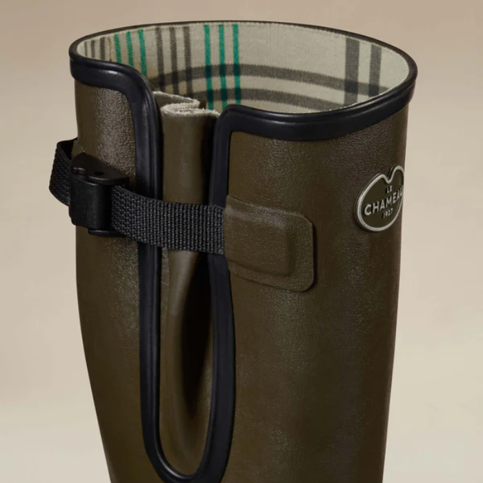 Brown wellington boot with a strap and visible brand logo on a beige background