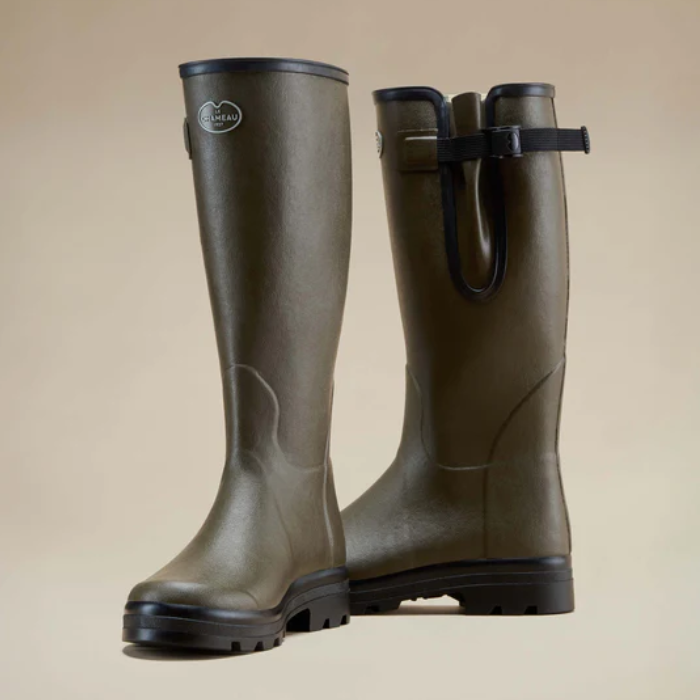 Pair of green rubber boots with a strap on a beige background