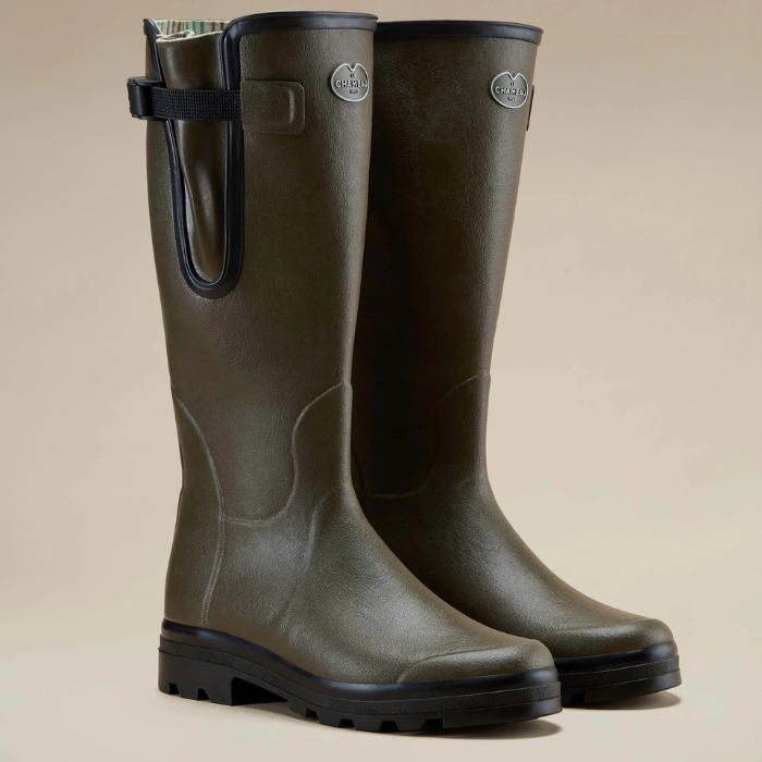 Pair of green rubber boots with black soles on a beige background