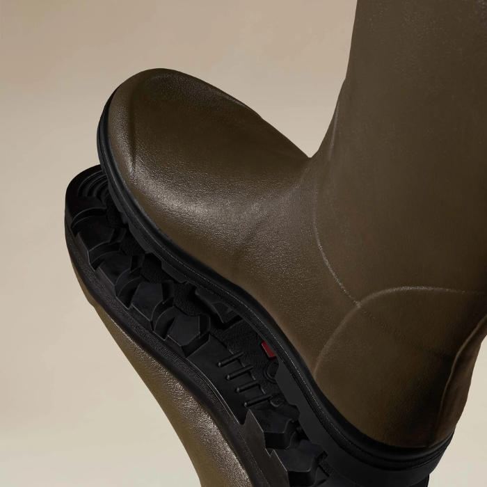 Green rubber boot with black sole on a beige background