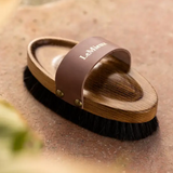 Horse grooming brush with brown handle and wooden head on a textured surface, featuring the brand 'LeMieux'.