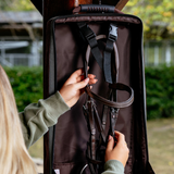 Person holding a bridle bag with a strap, outdoors.