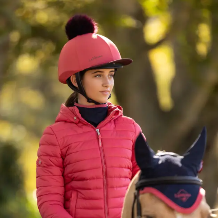 Person wearing a cranberry red helmet cover and jacket riding a horse with a blurred natural background