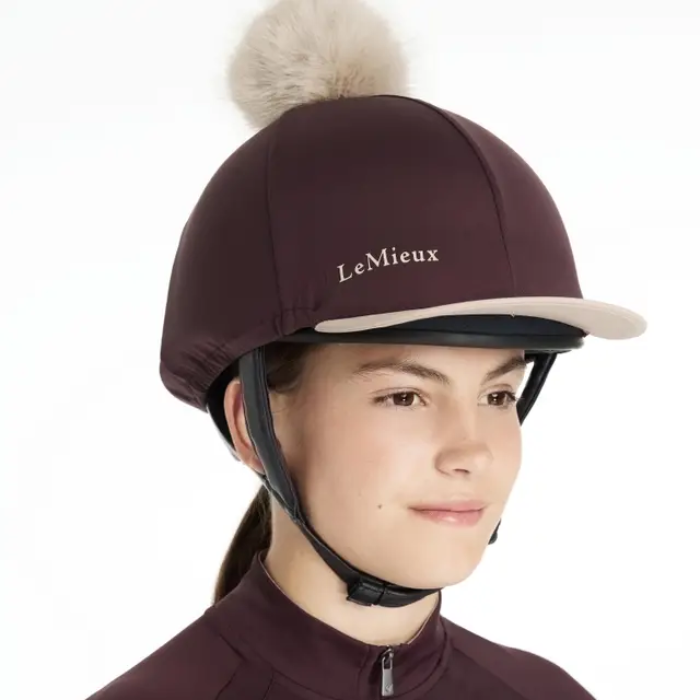 Person wearing a riding helmet, brown equestrian helmet cover with a pom-pom on a white background