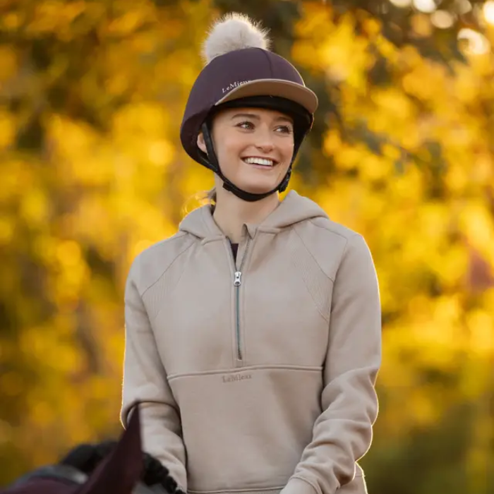 Person wearing a beige hoodie and helmet with a blurred autumn background