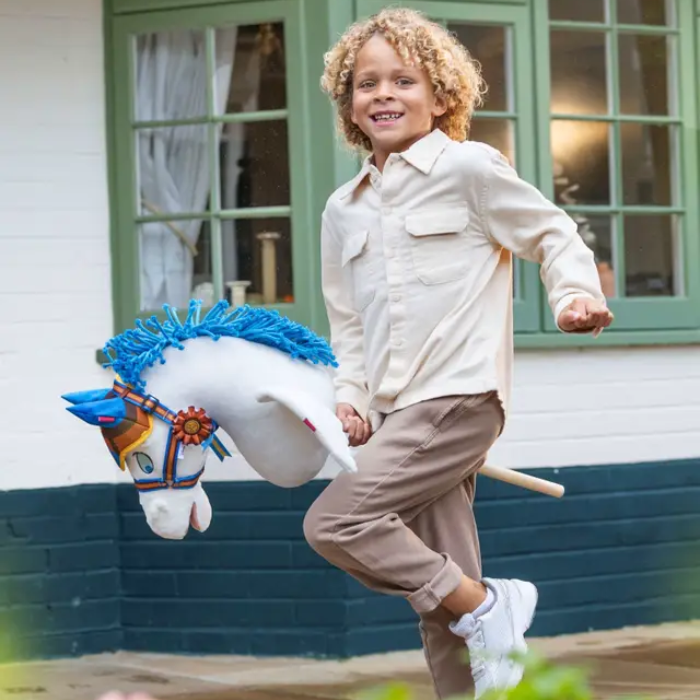 Child playing with a toy horse in front of a house