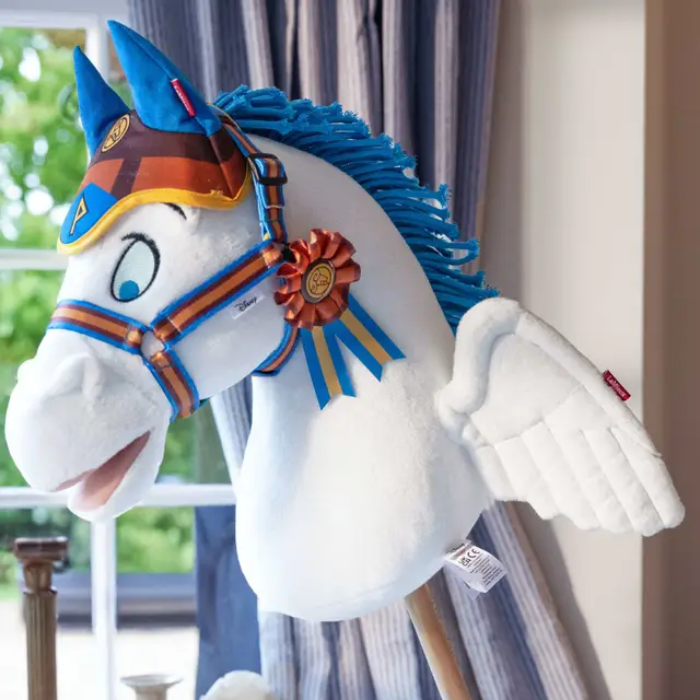 Plush toy horse with blue mane and decorative bridle in a room setting