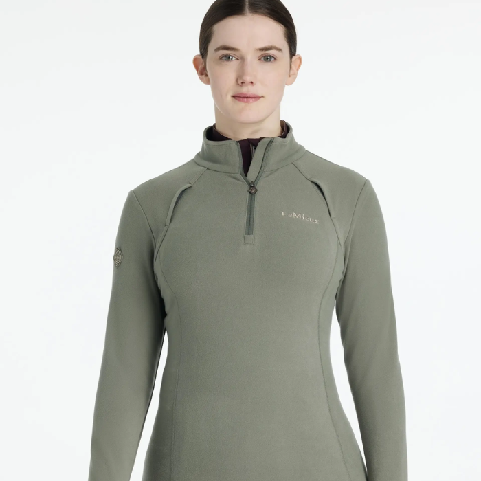 Woman wearing a green riding top with LeMieux brand logo on a white background