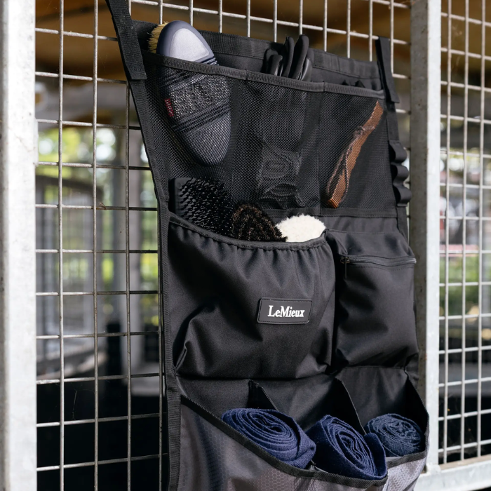 Hanging storage pockets in black with horse brushes and leg bandages in the pockets on a metal frame