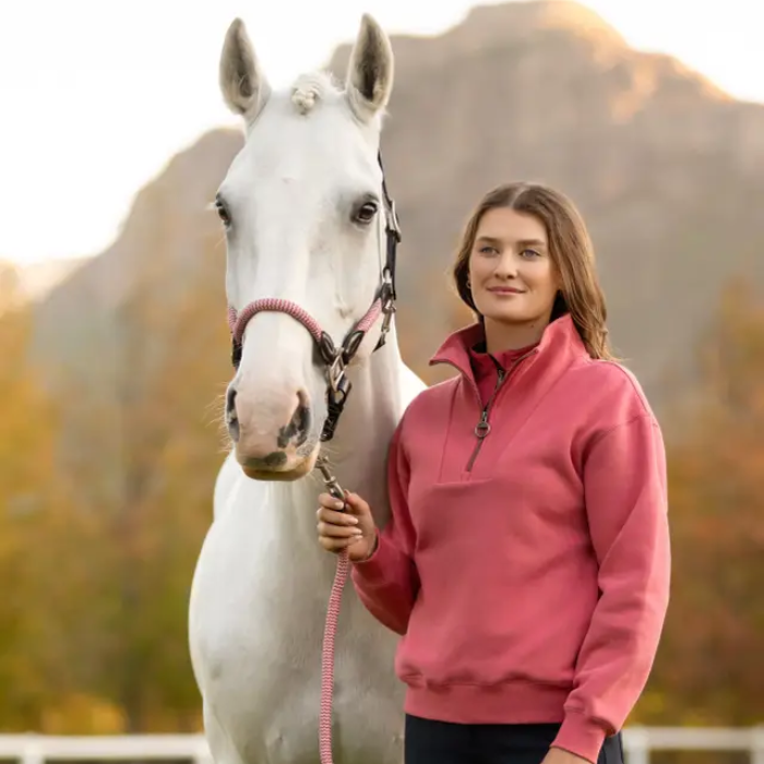 Woman in a cranberry sweater standing next to a white horse with a blurred background