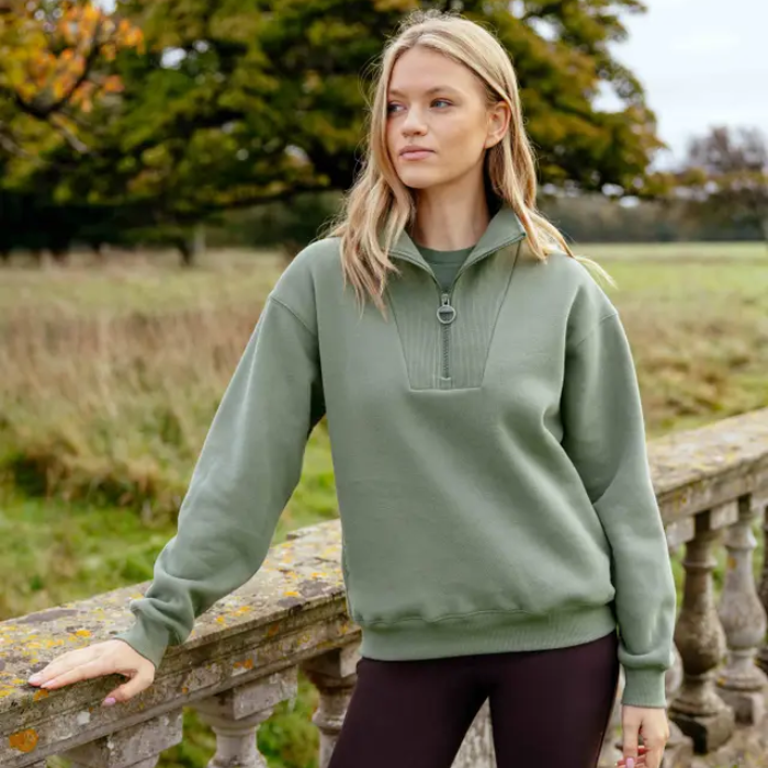 Woman wearing a green sweater standing outdoors with trees and grass in the background