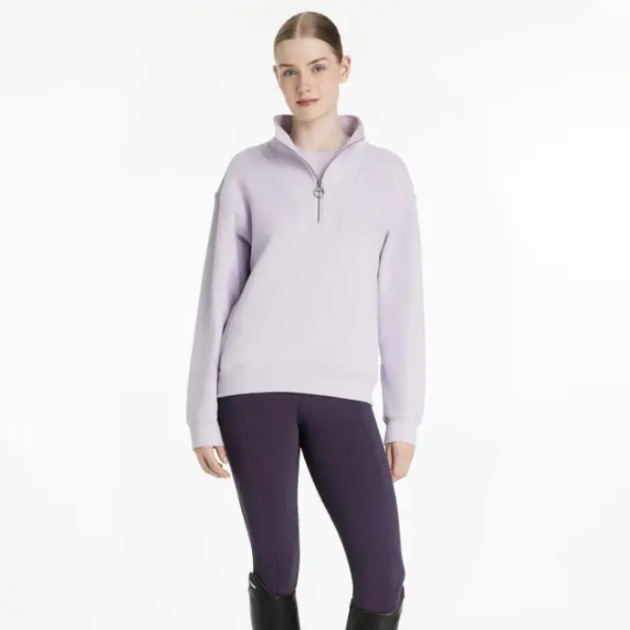 Woman wearing a light purple sweatshirt and dark purple riding leggings on a white background