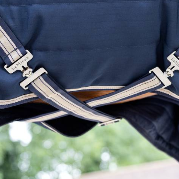 Close-up of a navy blue horse rug with beige straps and hardware, featuring the LeMieux brand.
