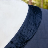 Navy blue horse rug with a fleece collar and blurred green background