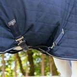 Navy quilted horse blanket with brand logo on a blurred green background