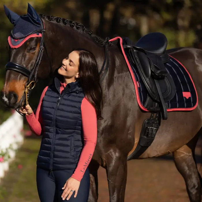 Woman in equestrian attire standing next to a horse with a saddle and bridle.