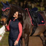 Woman in equestrian attire standing next to a horse with a saddle and bridle.