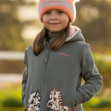 Child wearing a green jacket with horse designs and 'LeMieux' embroidered logo in natural setting.