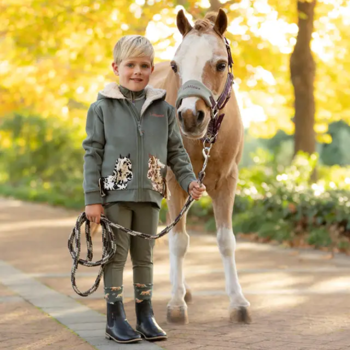 Child holding a horse's reins in an outdoor setting with trees in the background