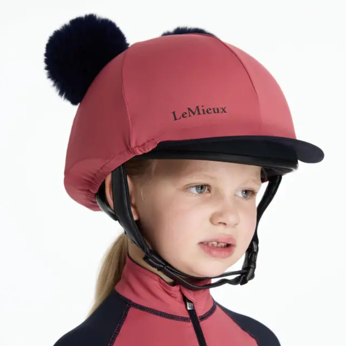 Child wearing a red equestrian helmet with black pom-poms on a white background