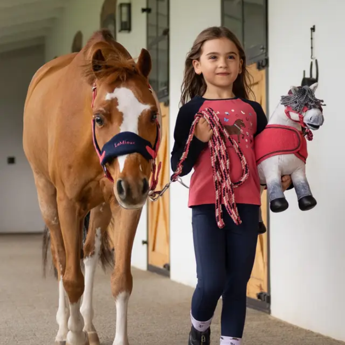 Girl holding a horse and a plush toy horse in a stable block setting