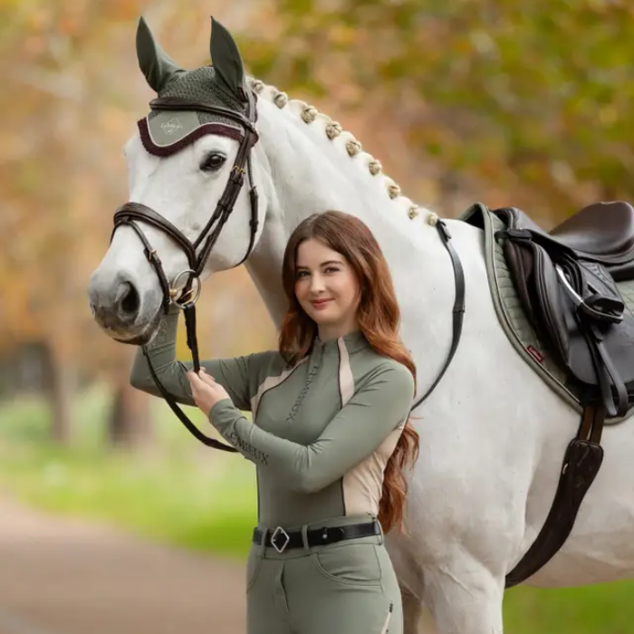 Woman in equestrian attire standing next to a white horse in an outdoor setting