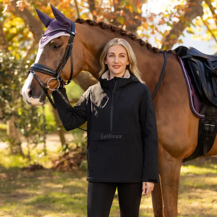 Woman standing next to a horse in an outdoor setting with trees in the background