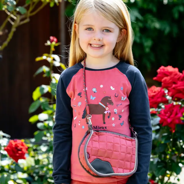 Young girl holding a pink equestrian bag with flowers in the background