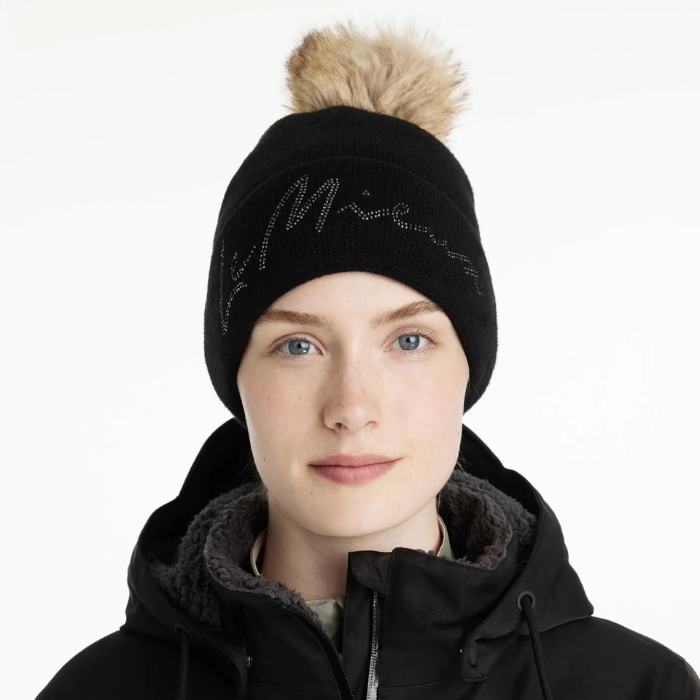 Person wearing a black beanie with a fur pom-pom and a black jacket on a white background