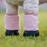 Close-up of a toy horse's legs with pink leg wraps on a grassy field.