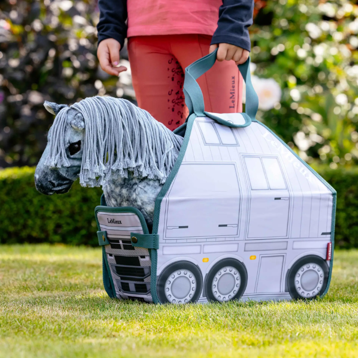Child holding a toy truck with a horse inside, outdoors.