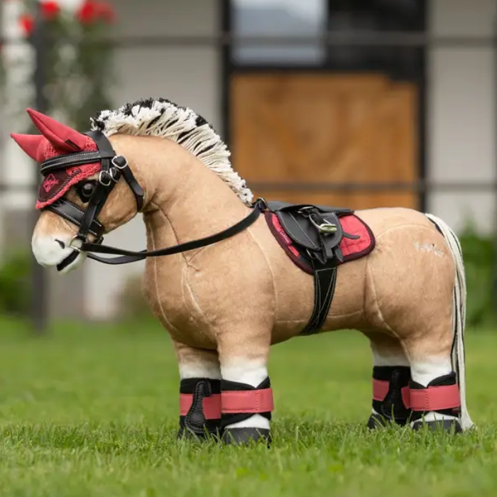 Plush toy horse with a red and black bridle on grass
