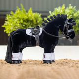 Black plush horse with a white saddle blanket and bridle on a sandy surface.