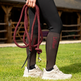 Person holding a red and black rope lead with a stable in the background