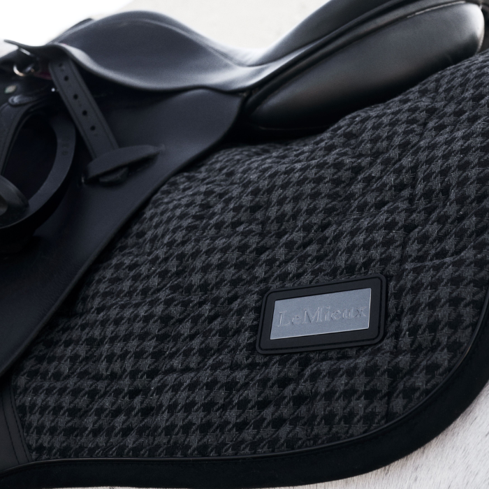 Close-up of a black and grey houndstooth-patterned saddle with a brand label on a white background.