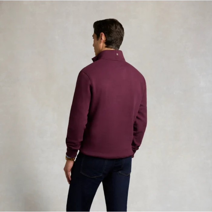 Holland Cooper Classic Quarter Zip Sweat (Men's) Variant Colour Mulberry. A male model wearing a mulberry coloured sweater and blue jeans on grey background.