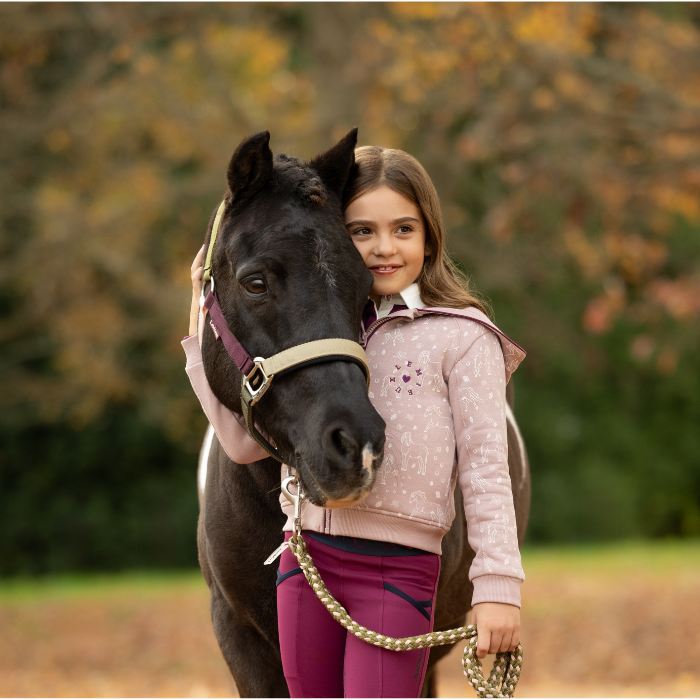 LeMieux AW26 Medley Headcollar Variant Colour Gooseberry/Pear/Petal. A dark coloured pony with a young person holding horse head. Horse is wearing gooseberry headcollar with matching lead rope and person with wearing pink top on faded autumn background.