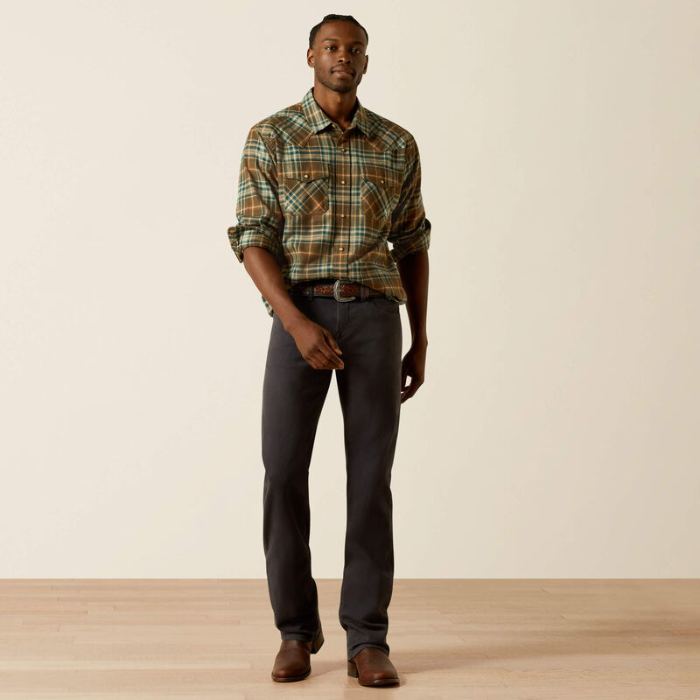 Man wearing a plaid shirt and dark jeans standing against a plain background