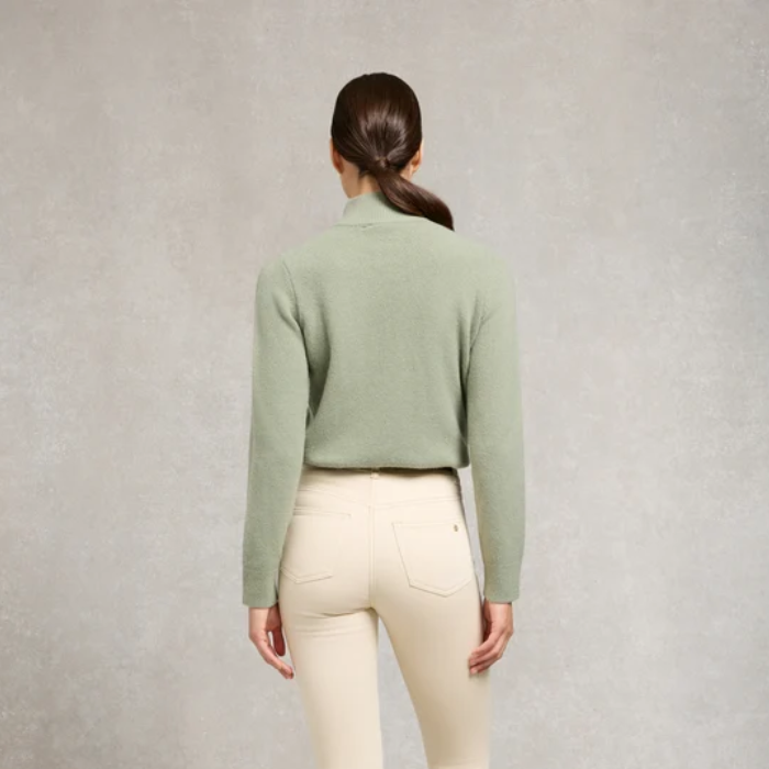 Holland Cooper Country Quarter Zip Knit Variant Colour Sage. A model wearing a sage green sweater, brown belt and cream trousers on grey background.