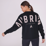Woman wears a black sweatshirt with AUBRION logo across the back