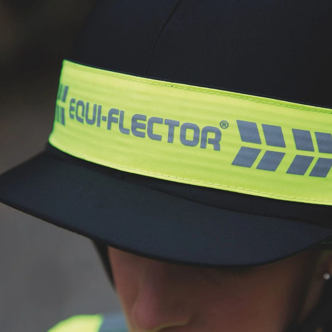 Close-up of a riding hat with a yellow band and visible 'EQUI-FLECTOR' logo on a blurred background